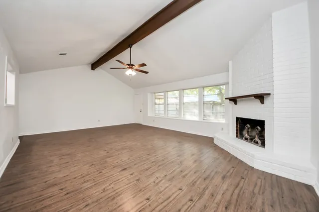 a view of an empty room with wooden floor fireplace and a window