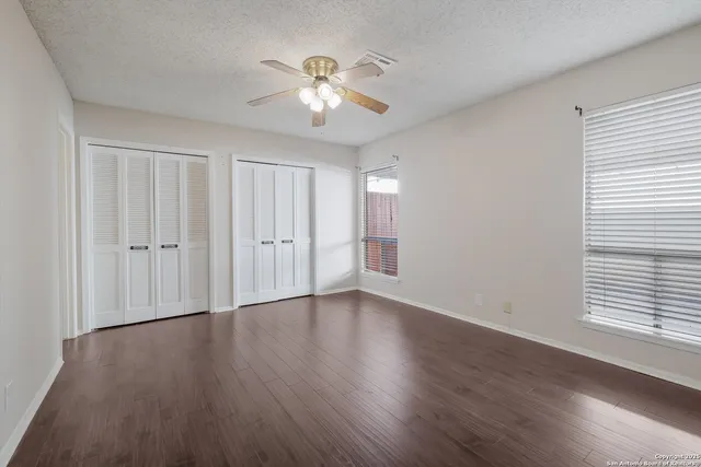 an empty room with wooden floor chandelier fan and windows