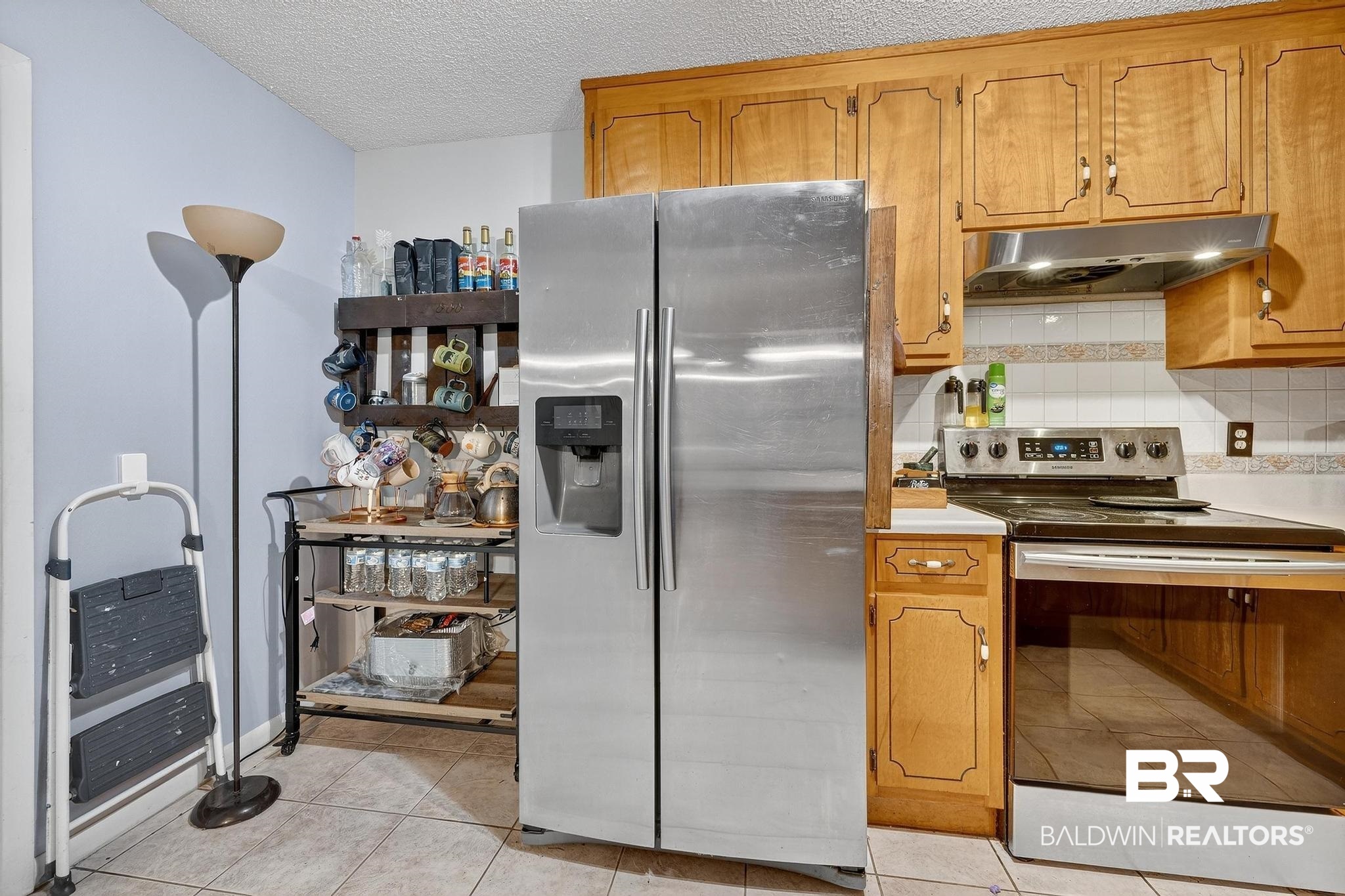 21895 2nd Street Silverhill, AL 36576 - Photo 23 of 43 Kitchen featuring appliances with stainless steel finishes, light tile floors, light countertops, under cabinet range hood, and backsplash
