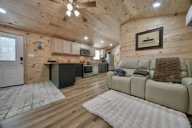 a large kitchen with stainless steel appliances granite countertop a large counter top a couches and a flat screen tv