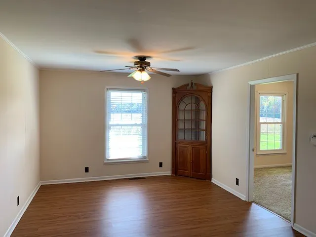 an empty room with wooden floor chandelier fan and windows