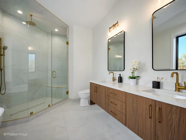 a spacious bathroom with double sink a toilet a mirror and shower