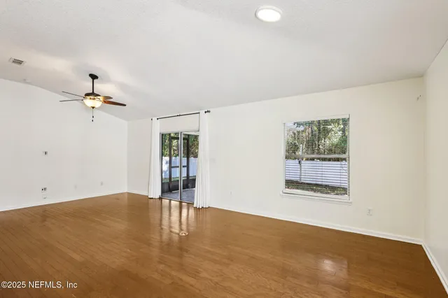 a view of an empty room with wooden floor and a kitchen
