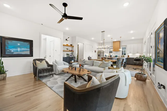 a living room with couches a coffee table and kitchen view with wooden floor