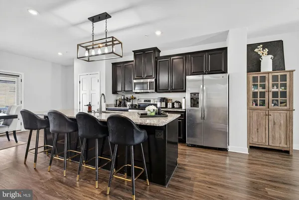 a kitchen with stainless steel appliances granite countertop a dining table chairs refrigerator and cabinets
