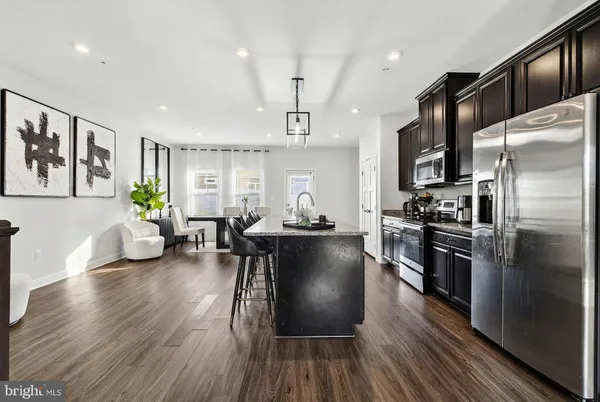 a living room with stainless steel appliances furniture wooden floor and a kitchen view