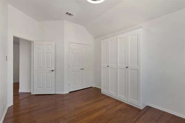 an empty room with wooden floor closet and windows