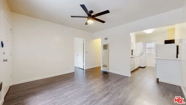 a view of an empty room with wooden floor and a ceiling fan
