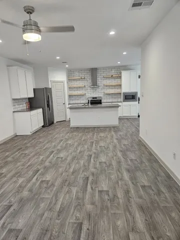 a large white kitchen with kitchen island a stove a refrigerator cabinets and living room view