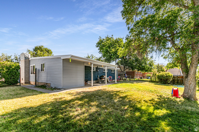 1619 Davis Drive Layton, UT 84041 - Photo 27 of 27 Expansive backyard featuring a large green lawn, mature shade trees, and a covered patio area with a light-colored roof