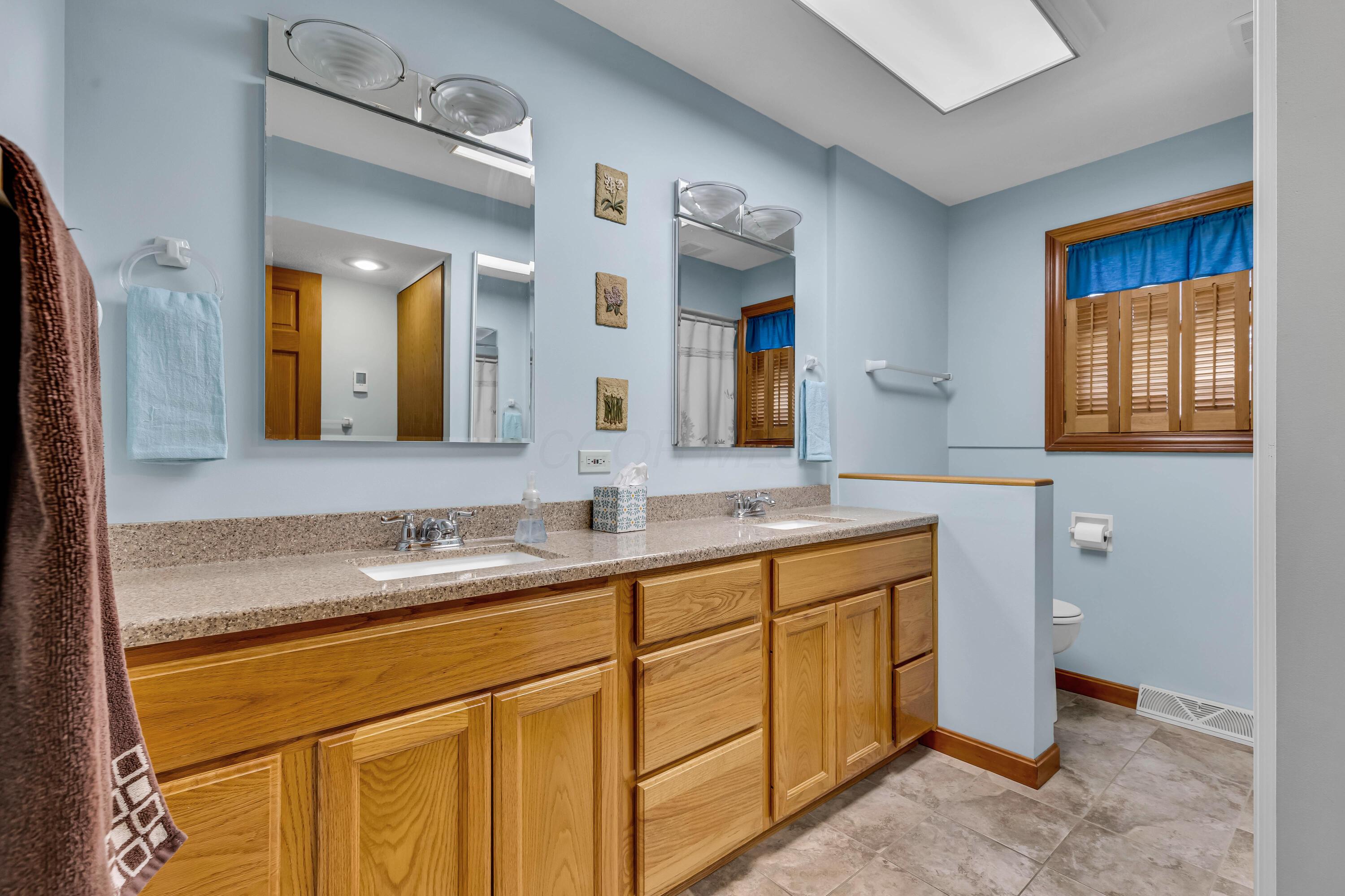 1213 East Cooke Road Columbus, OH 43224 - Photo 27 of 57 • Heated, ceramic tile flooring • Blue painted walls • Linen closet with bi-fold doors • Laundry chute • Enclosed vanity with double bowl, cultured marble sinktop • (2) 2 bulb wall lights • Ceiling light • Tub/shower combination with ceramic tile surround • Window shutters • (2) mirrored medicine cabinets