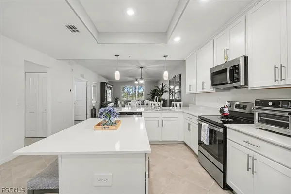 a kitchen with stainless steel appliances kitchen island granite countertop a sink dishwasher stove and white cabinets with wooden floor