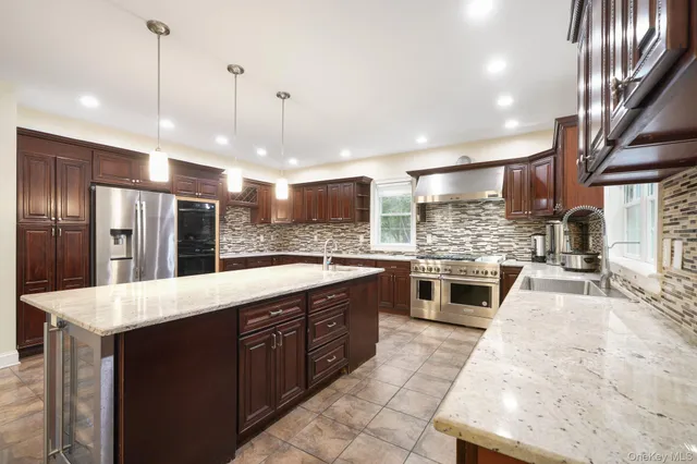 a large kitchen with stainless steel appliances granite countertop plenty wooden cabinets counter space a sink and a chandelier