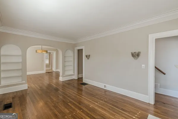 a view of an empty room with wooden floor and chandelier