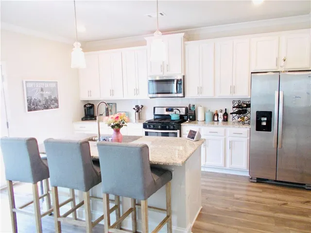 a kitchen with stainless steel appliances granite countertop a white cabinets a sink a stove a dining table and chairs
