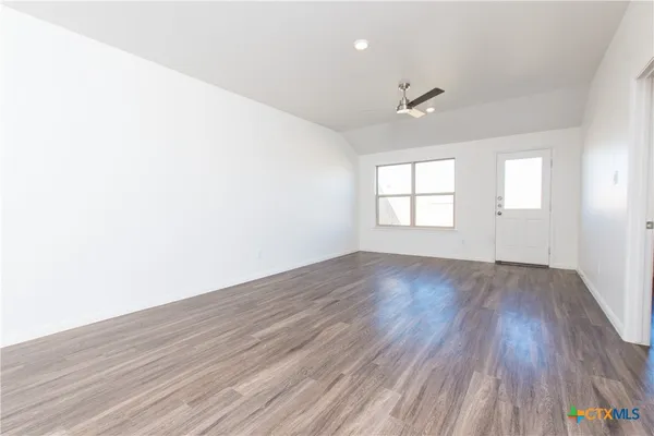 an empty room with wooden floor ceiling fan and windows