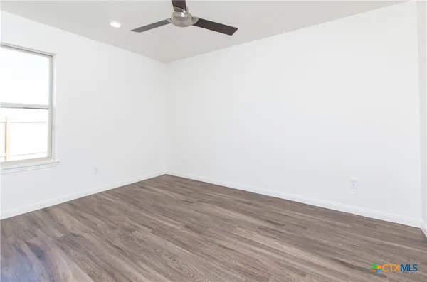 an empty room with wooden floor fan and windows