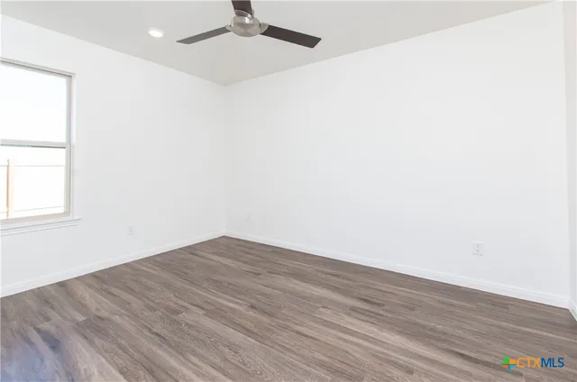 an empty room with wooden floor fan and windows
