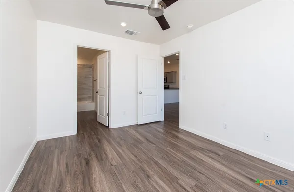an empty room with wooden floor ceiling fan and windows