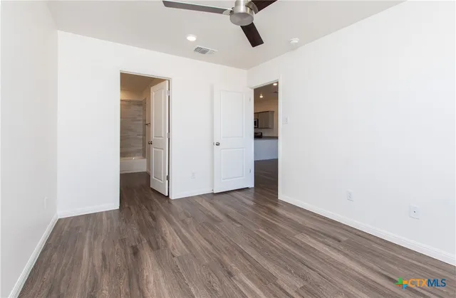 an empty room with wooden floor ceiling fan and windows