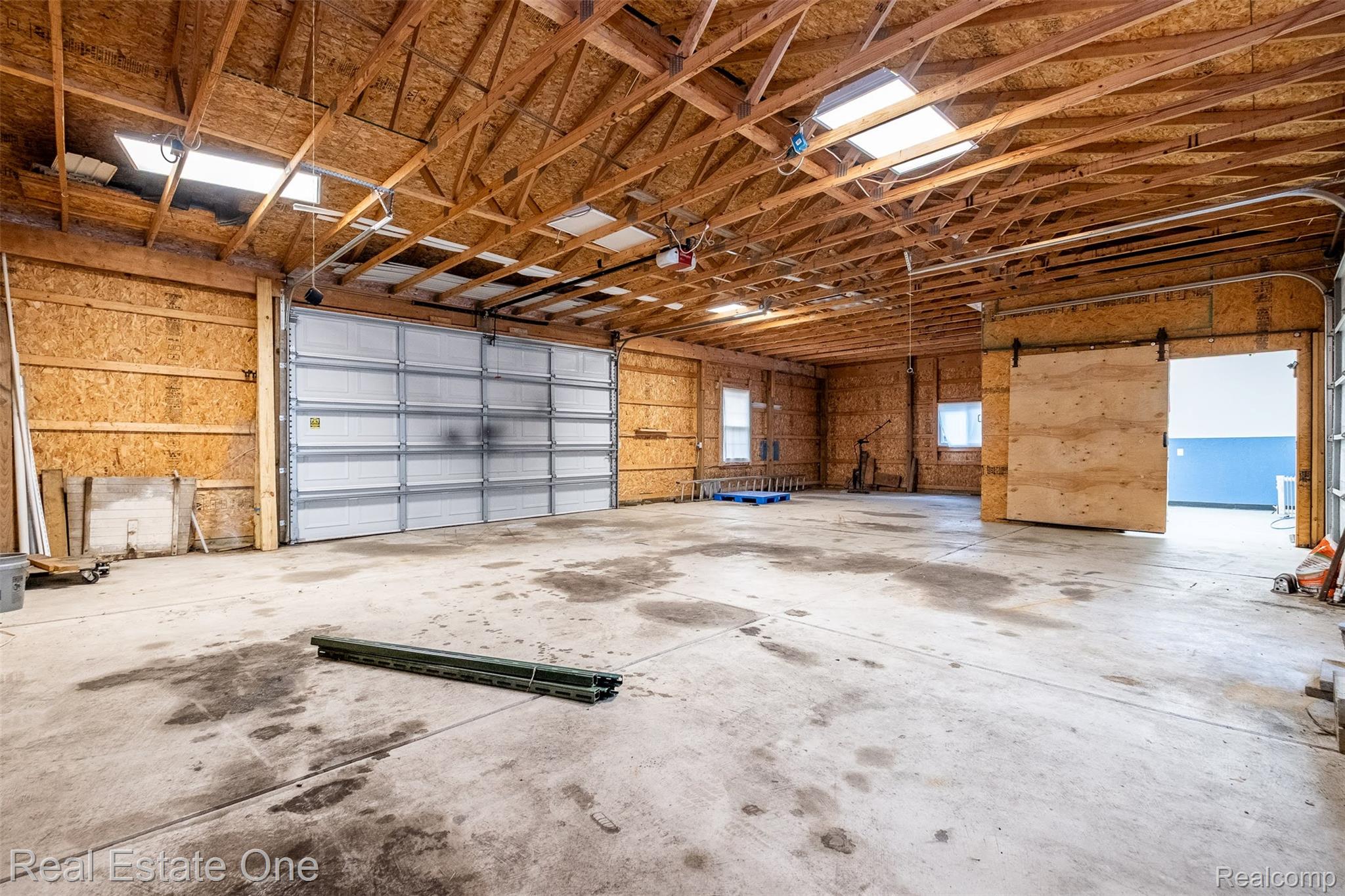 11030 Marshall Road South Lyon, MI 48178 - Photo 67 of 83 Spacious garage featuring exposed wood-beam ceiling with skylights, concrete flooring, overhead garage door with windows, and abundant natural light from multiple openings