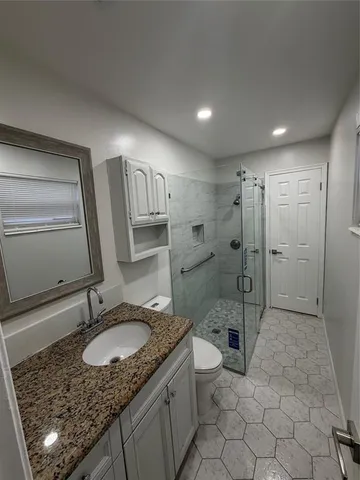 a bathroom with a granite countertop sink a toilet a mirror and shower