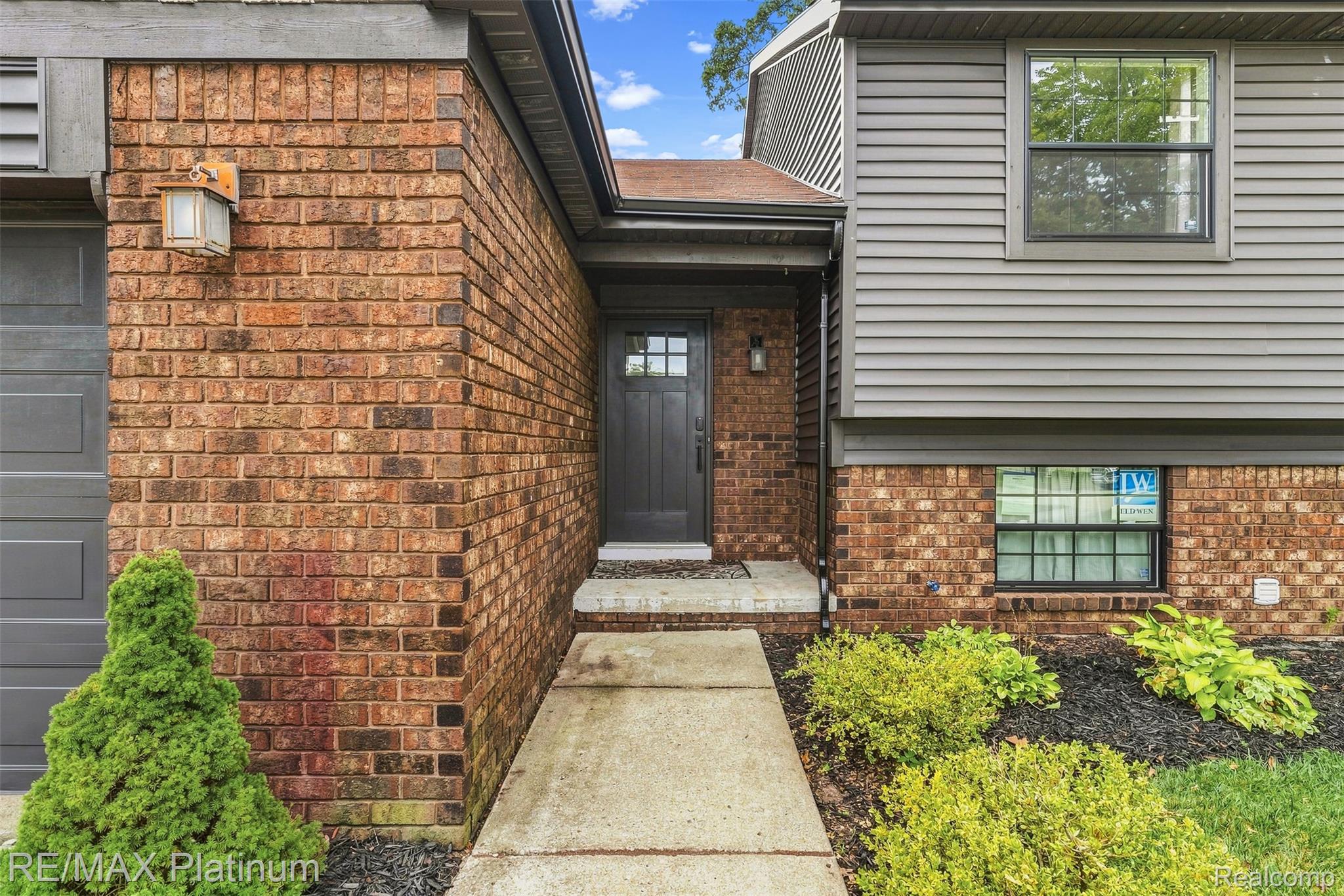 815 Oak Ridge Court Brighton, MI 48116 - Photo 4 of 37 Brick and horizontal siding exterior with a dark-paneled entry door, concrete walkway, and established landscaping