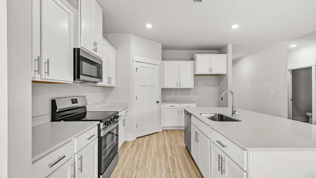 a kitchen with a sink dishwasher stove and white cabinets with wooden floor