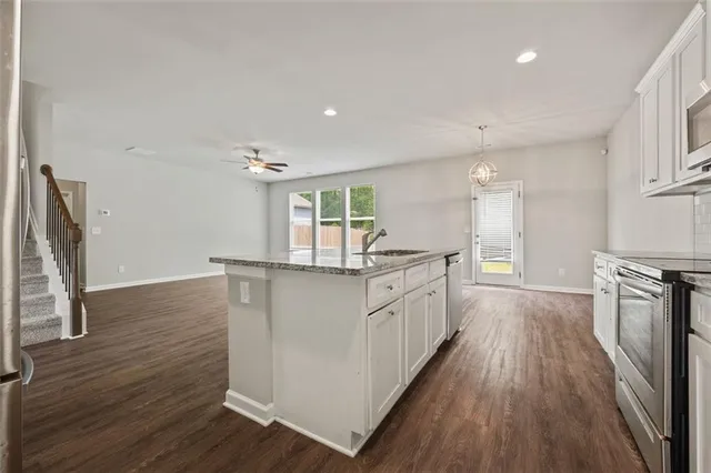 a kitchen with granite countertop a stove top oven a sink dishwasher and a refrigerator with wooden floor