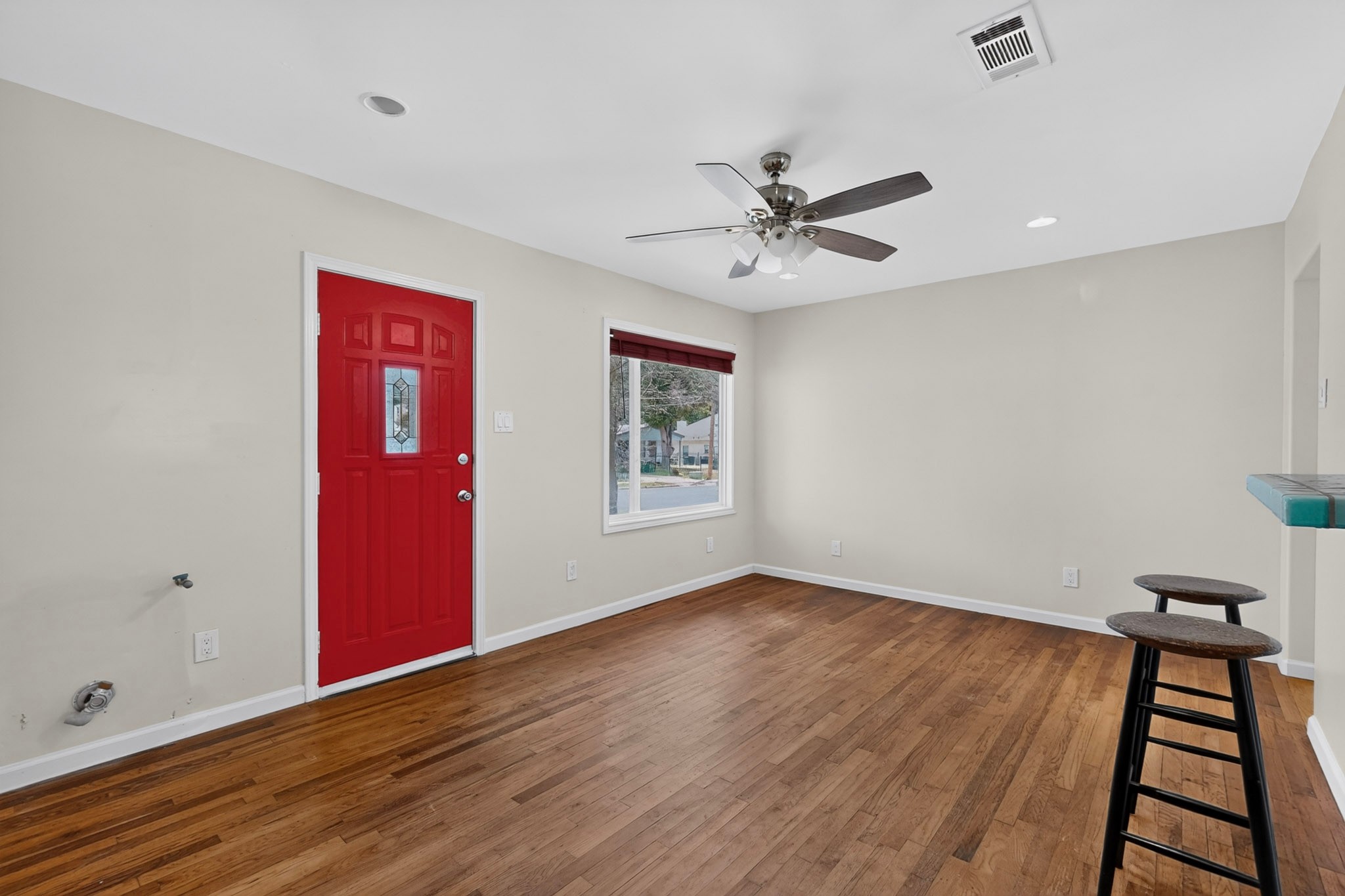 4711 Alf Avenue Austin, TX 78721 - Photo 4 of 34 A vibrant red front door welcomes you into this naturally illuminated living space, showcasing rich hardwood flooring and a stylish ceiling fan.