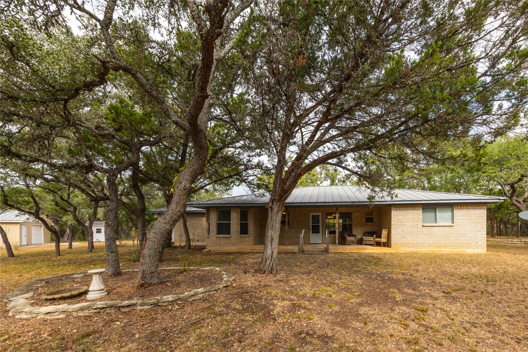 2501 Fischer Store Road Wimberley, TX 78676 - Photo 12 of 23 Expansive backyard featuring mature trees, a stone-lined planter, and a light-colored brick exterior