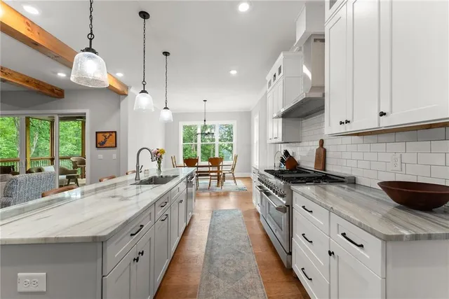 a kitchen with stainless steel appliances kitchen island granite countertop a stove top oven a sink dishwasher a refrigerator white cabinets and couches with wooden floor