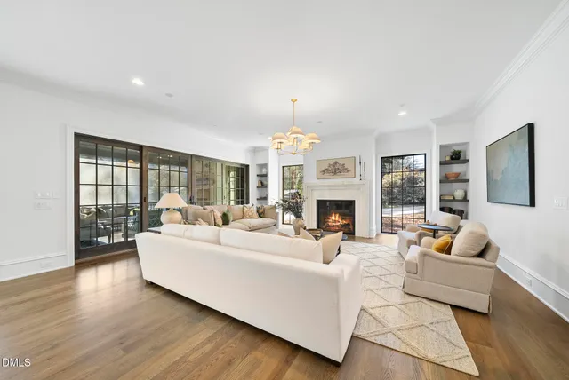 a living room with large couches chandelier and a dining table with wooden floor