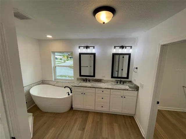a spacious bathroom with double vanity sink a mirror a bathtub and a window