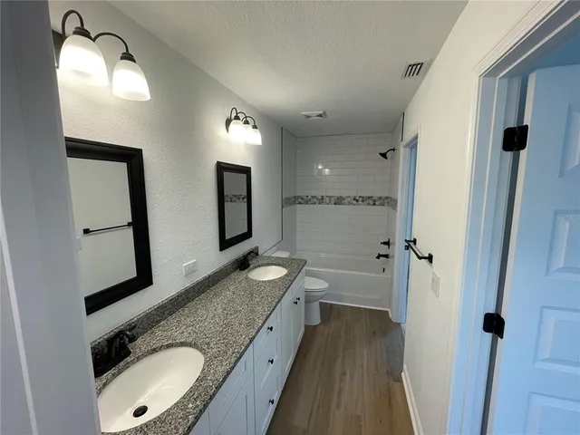 a bathroom with a granite countertop double vanity sink and mirror with shower