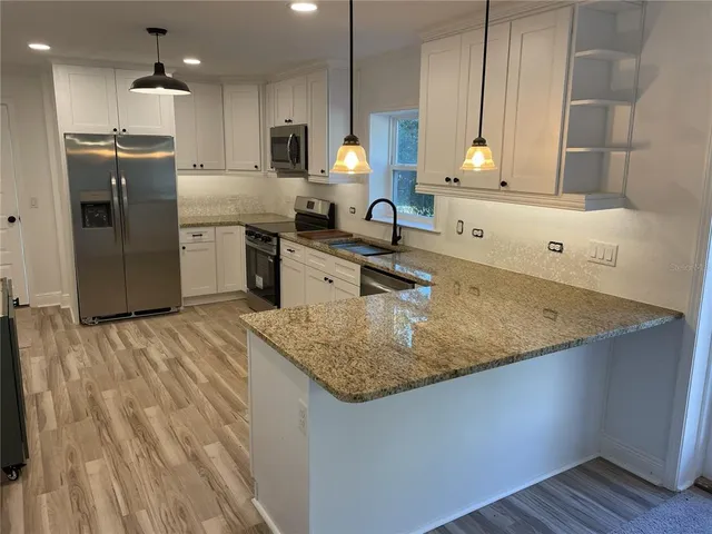 a kitchen with stainless steel appliances granite countertop a sink dishwasher and a refrigerator with wooden floor