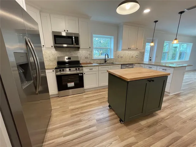 a kitchen with stainless steel appliances granite countertop a stove a sink dishwasher a refrigerator and a oven with wooden floor