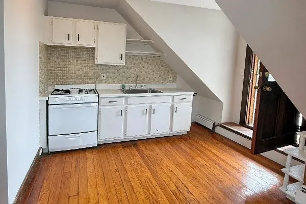 a kitchen with stainless steel appliances granite countertop a sink a stove oven and white cabinets with wooden floor
