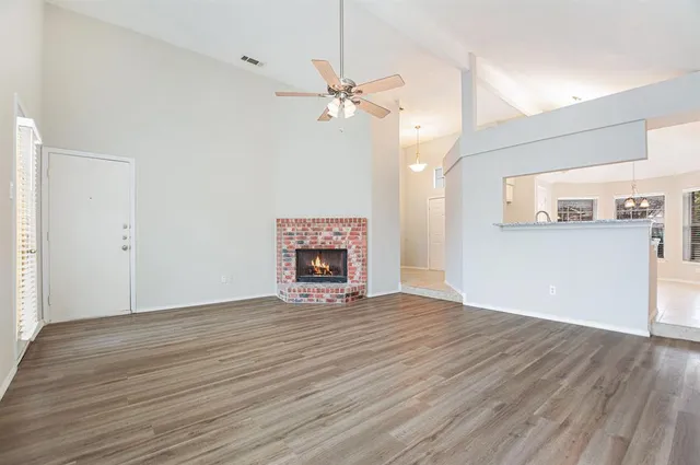 an empty room with wooden floor fireplace and windows