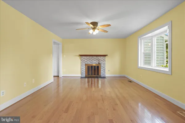 a view of an empty room with wooden floor and a ceiling fan