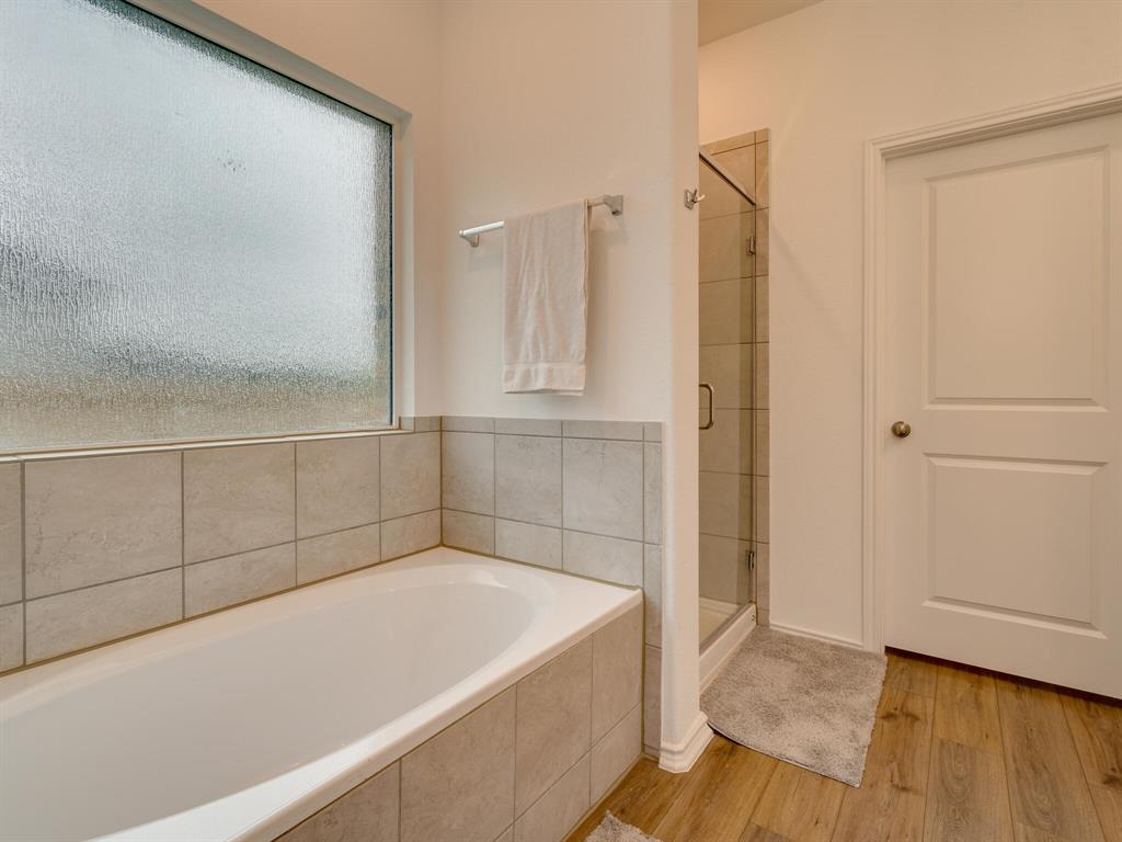 1208 Sweetspire Street Leander, TX 78641 - Photo 16 of 36 White bathtub with surrounding tile wainscoting, a frosted rectangular window, and wood-finish flooring