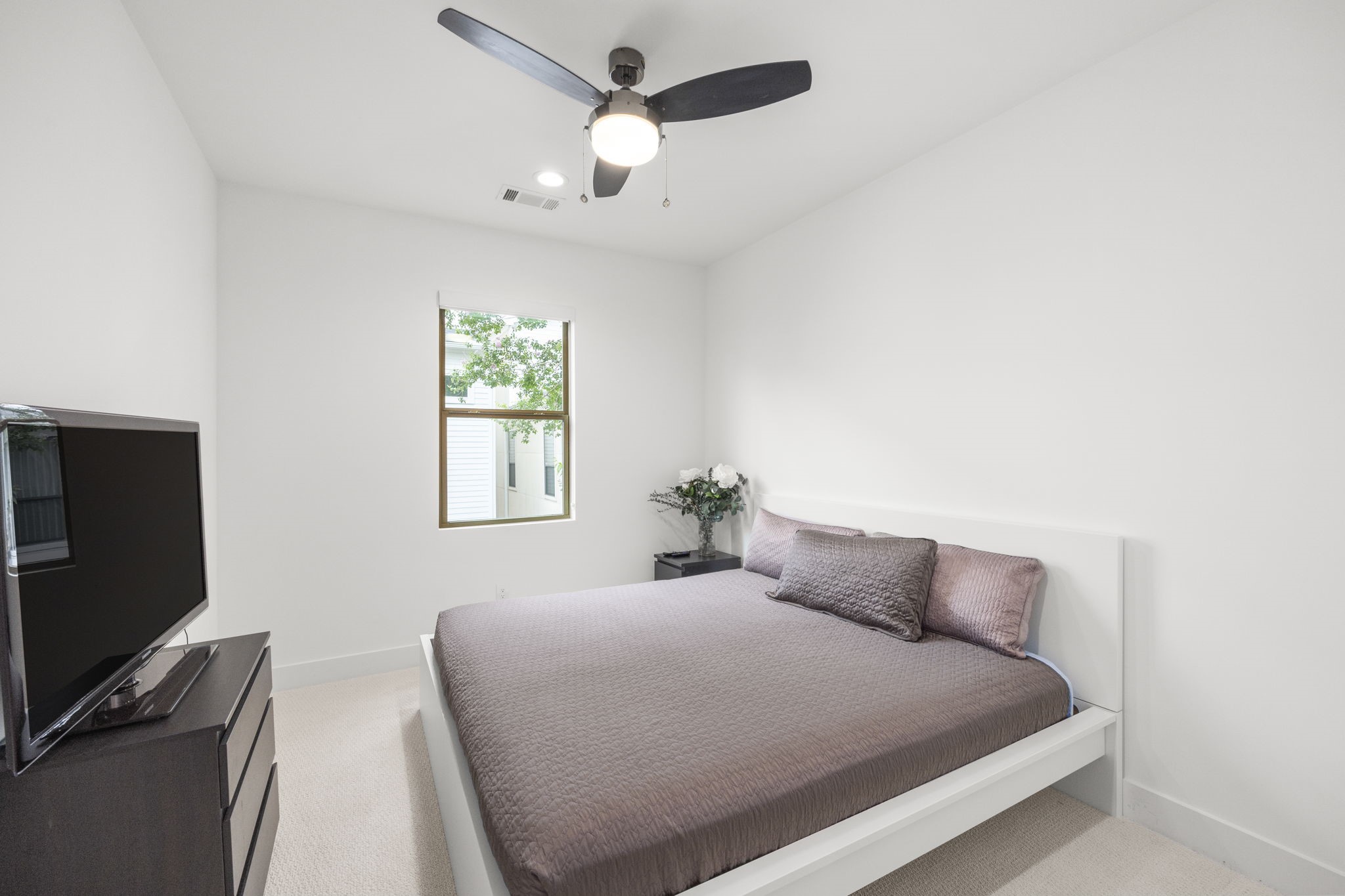 2411 Hazard Street Houston, TX 77019 - Photo 36 of 46 This secondary bedroom offers a spacious and serene retreat, featuring soft neutral tones, plush carpeting, and a ceiling fan for comfort. A large window provides natural light, enhancing the room's bright and airy feel.