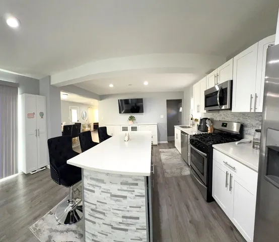 a open kitchen with stainless steel appliances kitchen island granite countertop a stove top oven a sink dishwasher a dining table and chairs with wooden floor