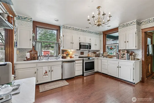 a kitchen with stainless steel appliances granite countertop a refrigerator a sink dishwasher a stove a dining table and chairs with wooden floor
