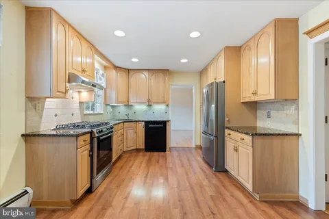 a large kitchen with stainless steel appliances granite countertop a stove a sink dishwasher and a refrigerator with wooden floor