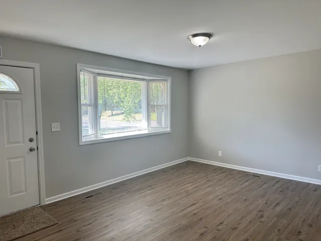 a view of an empty room with wooden floor and a window