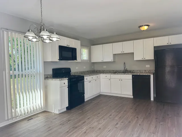 a kitchen with stainless steel appliances granite countertop a refrigerator a sink dishwasher a stove and white cabinets with wooden floor