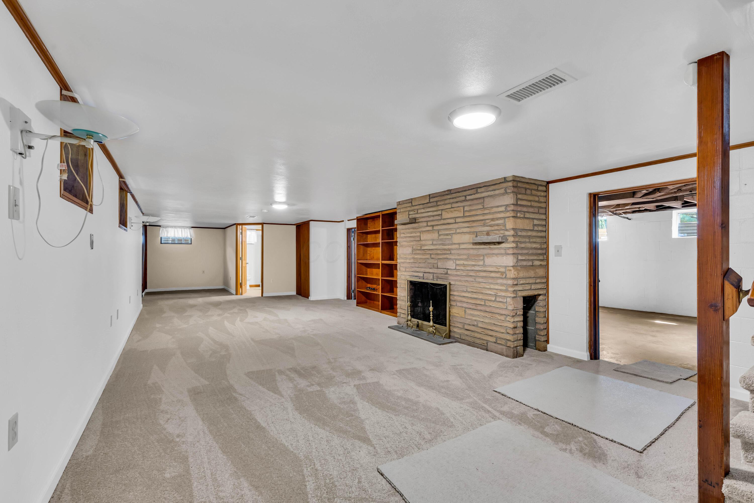 1213 East Cooke Road Columbus, OH 43224 - Photo 38 of 57 • New light sand carpet ~ 2025 • Ivory painted walls • (2) ceiling lights • Lighted wall sconces • Glass block windows • Stone fireplace with log chamber • Built-in bookcases • Lighted walk-in canning room • Closet with double sliding doors