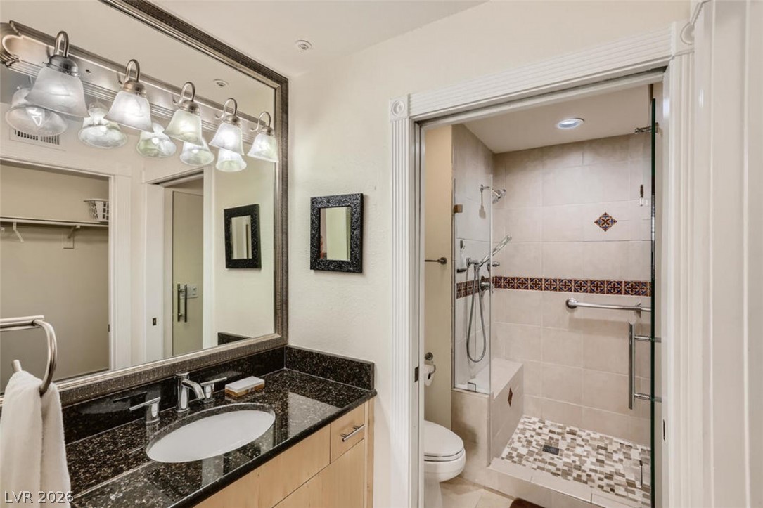 210 East Flamingo Road, Unit 137 Las Vegas, NV 89169 - Photo 20 of 32 A well-appointed bathroom offers a functional vanity with dark granite counters and a glass-enclosed shower with decorative tile.
