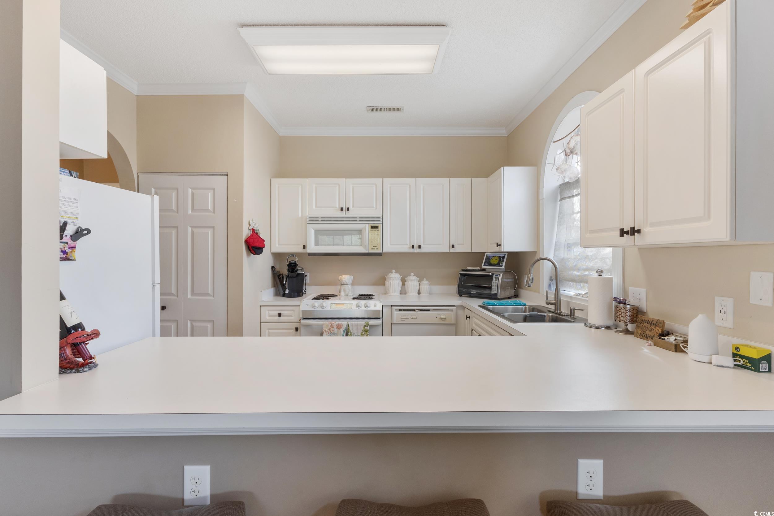 4781 Wild Iris Drive, Unit 301 Myrtle Beach, SC 29577 - Photo 12 of 33 Kitchen with ornamental molding, white appliances, light countertops, and a breakfast bar